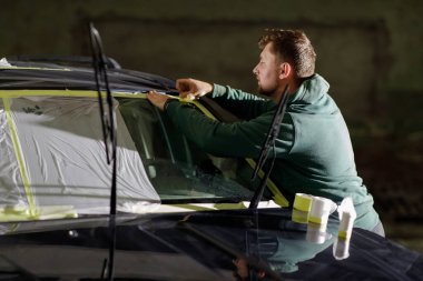 Profesyonel bir araba boyamadan önce bir aracın alanlarını kaydetmeye odaklanır. Çalışma alanı loş, otomotiv bakımına ilişkin ayrıntılı hazırlıkları vurguluyor.