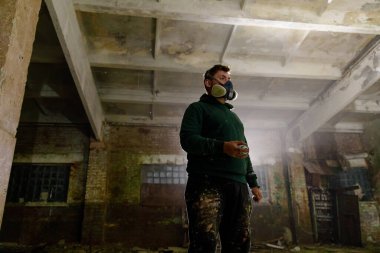 Terk edilmiş bir depoda duran bir şehir sanatçısı, resim yapmak için sprey boya kullanıyor. Koruyucu bir maske takan sanatçı, yaratıcılık sürecini gözler önüne seren toz ve molozlarla çevrilidir..