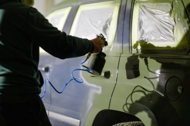 Bir işçi, iyi aydınlatılmış bir garajda sprey tabanca kullanarak bir araca boya sürüyor. Süreç ayrıntılara dikkat ve yeni bir bitiş için dikkatli bir hazırlık vurguluyor.