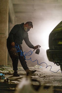 Bir sanatçı bakımsız bir depoda, renkli sprey boyaları arabaya sürerek özenle çalışır. Bu kentsel sanat ortamında yaratıcılık akarken toz havayı dolduruyor..