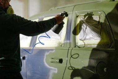 Bir teknisyen iyi donanımlı bir garajda arabanın üzerine sprey boya sıkar. Atmosfer, restorasyon çalışmaları sırasında kalite ve işçiliğe odaklandığını gösteriyor..