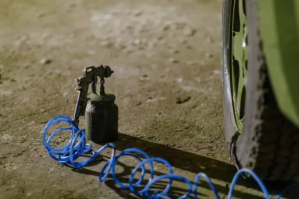 Kirli bir yüzeyde patlak bir lastiğin yanında duran bir lastik onarım aleti. Mavi hava hortumu yere yayılıyor. Bu da geceleri düşük ışık alan bir ortamda devam eden bir çalışmayı gösteriyor..