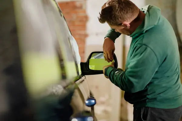 Yetenekli bir tamirci garajdaki bir aracın dikiz aynasını dikkatlice değiştiriyor. Görevler, kalite onarımı için hassas düzenlemeler ve adanmış bir iş etiğini içeriyor.
