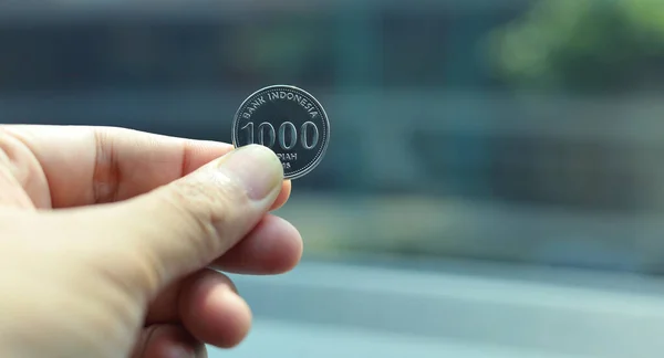 Bin rupia sikke, bulanık bir arkaplanda izole edilmiş bir rupia sikkesi tutan insan eli. Endonezya Rupisi