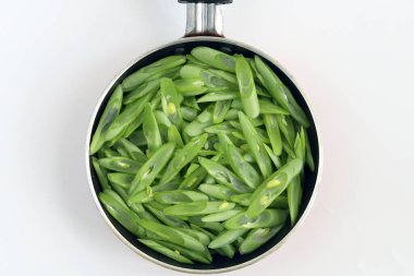 Kızartma tavasındaki çiğ yeşil fasulye beyaz arka planda izole edilmiş.