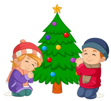 Noel günü dizlerinin üzerinde dua eden iki küçük çocuk. Resmin arkasında büyük bir Noel ağacı var.