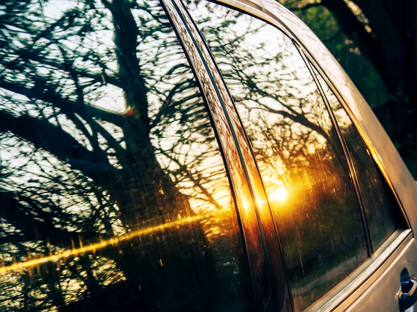 Sunset behind the window of a car. The sun is reflected in the glass. Reflection of trees in a car window at sunset. Blurred background. Reflection of trees in the window glass of a car at sunset.