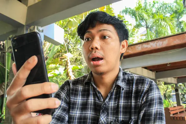 Scioccato Giovane Uomo Asiatico Guardando Telefono Nero Mentre Seduto Nei — Foto Stock