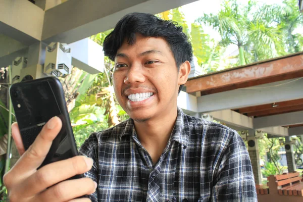 아시아인 남자는 휴대폰을 보면서 행복하고 흥분된 몸짓을 치아로 웃었다 플란넬 — 스톡 사진