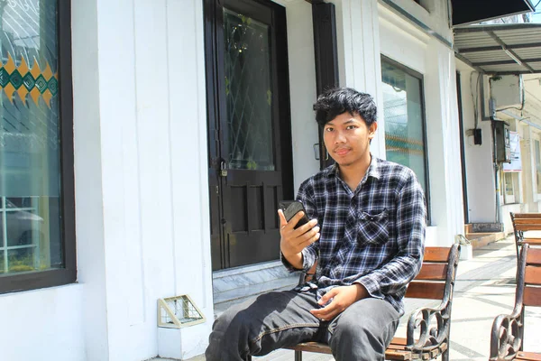 Mutlu Asyalı Genç Adam Akıllı Telefonu Tutuyor Otururken Kameraya Bakıyor — Stok fotoğraf