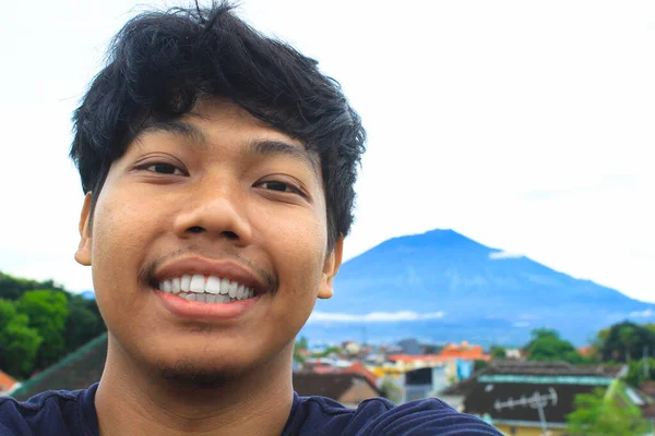 一位兴奋的亚洲年轻人背包客在印尼徒步旅行时 拍下了一张背景为Arjuna Mount的自拍照片 — 图库照片