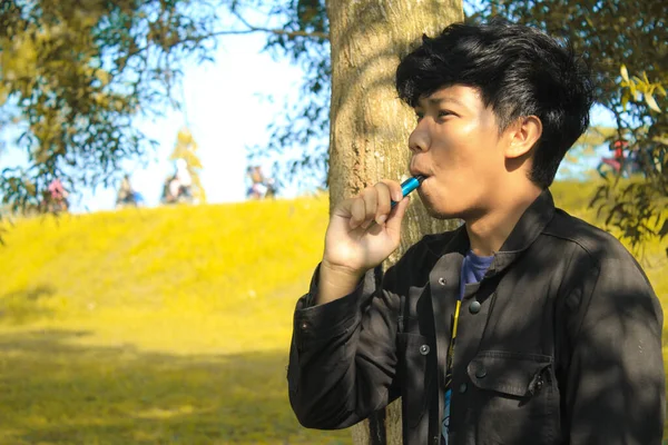 リラックスした若いアジアの男は黒のジャケットを身に着けている満足した顔と木の牧草地の自然背景と青い空のポッドシステム — ストック写真