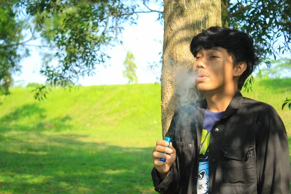 Расслабленный Молодой Азиат Дует Стручок Системы Вырабатывает Облако Туман Деревьями — стоковое фото