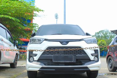 Beyaz SUV 'un ön görüntüsü ya da paslı zincir bariyerli galeri otoparkındaki çapraz araba.