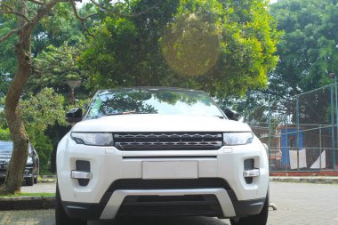 Tenis kortunun yanına park edilmiş beyaz çapraz araba manzarası. Yeşil ağaçlı bir arazi aracı.