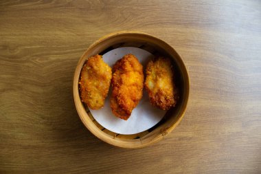 Tahta masadaki bambu kabında servis edilen altın sarısı kızarmış karides. Asya karidesli Çin yemeği.