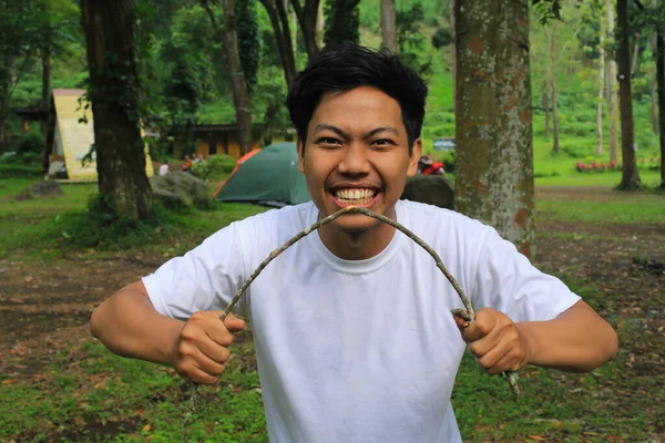 怒气冲冲的亚洲年轻人穿着白衬衫在热带森林里折断了树枝 — 图库照片