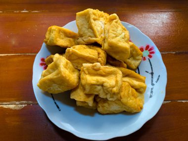 Kızarmış tofu beyaz tabakta servis edilir ve ahşap masanın üzerinde çiçek dürtüsü vardır. en üstteki görünüm