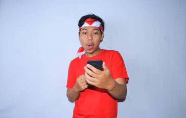 Endonezya 'nın bağımsızlık gününde kırmızı tişört ve saç bandı takan mutlu Endonezyalı genç adam cep telefonuna baktıktan sonra şok oldu.