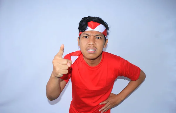 インドネシア独立記念日に赤いTシャツとヘッドバンドを着用しているカメラに彼のフォーフィンガーを指差す怒っているインドネシアの若者 — ストック写真