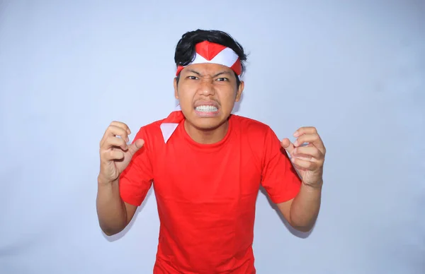 怒っているインドネシアの男は激しく叫んで インドネシア独立記念日に赤いTシャツとヘッドバンドを着て手を絞っている — ストック写真