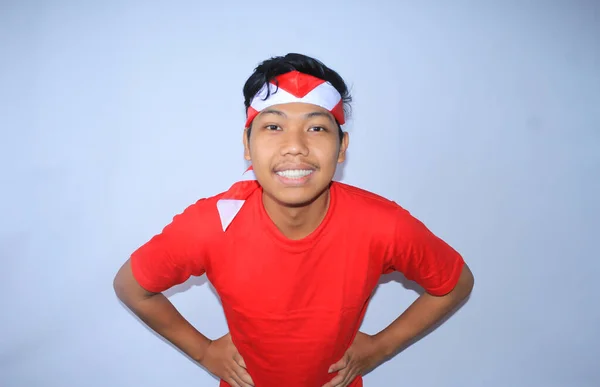 インドネシアの若い男性は 赤いTシャツとヘッドバンドを着て インドネシアの独立記念日を祝うウエストの手で笑っています カメラを見ています — ストック写真