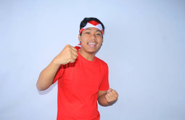 为庆祝他在印度尼西亚独立日的成功或目标 这位兴奋的印度年轻人举起了拳头 身穿红色T恤和头带 年轻人对自己的成就和满足表现出肯定的姿态 — 图库照片