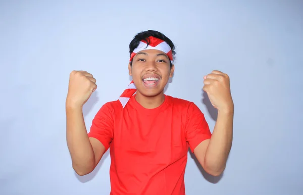 为庆祝他在印度尼西亚独立日的成功或目标 这位兴奋的印度年轻人举起了拳头 身穿红色T恤和头带 年轻人对自己的成就和满足表现出肯定的姿态 — 图库照片