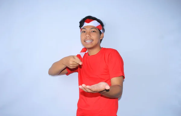 为庆祝印度尼西亚独立日 印度尼西亚男人用左手指着右手张开的手掌 身穿红色T恤 微笑着的画像 看着相机 — 图库照片