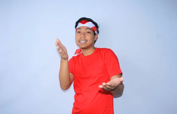 インドネシアの若い成人男性は想像上の製品を示しているか 赤いTシャツとインドネシアの独立記念日にインドネシアの独立記念日に赤いTシャツとインドネシアの国旗ヘッドバンドを着て平和で幸せな顔を提示しています — ストック写真