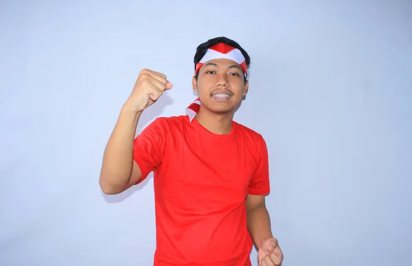 幸せなインドネシアの若い成人は 赤いTシャツとインドネシアの国旗ヘッドバンドを身に着けている平和的な顔で彼の勝利のための勝利をし 彼の拳をラスタリング — ストック写真