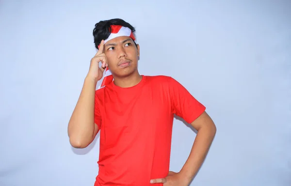 インドネシアの若い男性は インドネシア独立記念日に赤いTシャツとヘッドバンドを身に着けている頭で創造的なアイデアを考えてブレインストーミング — ストック写真