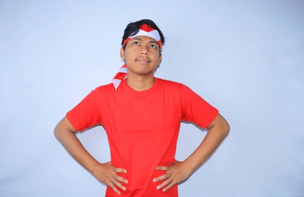 若い好奇心旺盛なインドネシアの男は 腰に手で考え 赤いTシャツとインドネシアの国旗ヘッドバンドを身に着けている一見 — ストック写真