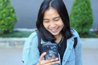 Neşeli Asyalı uzaktan kumandalı kadın gülerek sosyal medyada akıllı telefon sörfü, mobil uygulama, görüntülü sohbet, şehir merdivenlerinde yürürken internet indirimi.