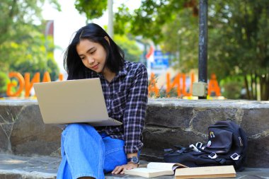 Genç gülümseyen Asyalı kadın dizüstü bilgisayar kullanıyor ve not defteri yazıyor. Neşeli Asyalı öğrenci Webinar izliyor ve dersini çalışıyor.