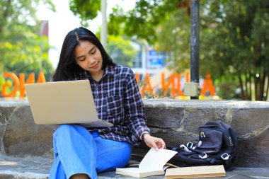 Genç gülümseyen Asyalı kadın dizüstü bilgisayar kullanıyor ve not defteri yazıyor. Neşeli Asyalı öğrenci Webinar izliyor ve dersini çalışıyor.