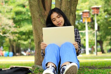 Genç gülümseyen Asyalı kadın dizüstü bilgisayar kullanıyor ve not defteri yazıyor. Neşeli Asyalı öğrenci Webinar izliyor ve dersini çalışıyor.