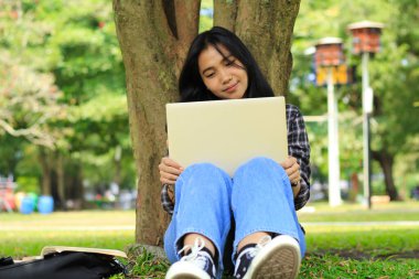 Genç gülümseyen Asyalı kadın dizüstü bilgisayar kullanıyor ve not defteri yazıyor. Neşeli Asyalı öğrenci Webinar izliyor ve dersini çalışıyor.