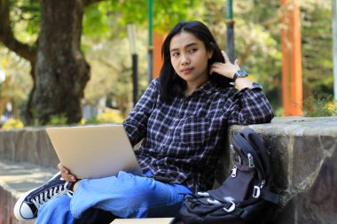 Mutlu Asyalı kadın gülümsemesi dışarıda çalışma alanında dizüstü bilgisayarla çalışmanın keyfini çıkar.