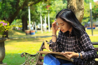 Asyalı genç bir kadının açık havada kalemle bir fikir ve yazı yazması kafasını karıştırıyor.