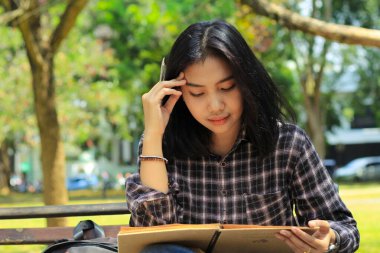 Asyalı genç bir kadının açık havada kalemle bir fikir ve yazı yazması kafasını karıştırıyor.