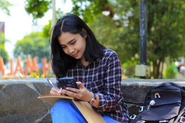 Mutlu ve neşeli Asyalı genç işçiler gülümseyen cep telefonu tutan, deftere veya günlüğe yazan, öğrenci öğrenen