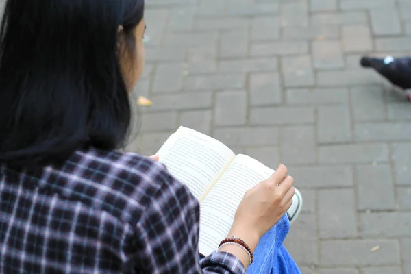 Mutlu, düşünceli Asyalı bir üniversite öğrencisi parkta kitap okuyor, eğitim konsepti.