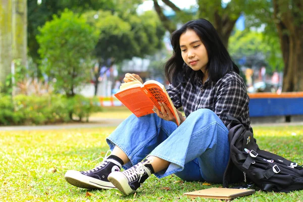 happy and succes female asian college student enjoying read a book in the park