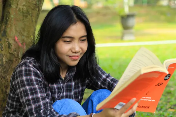 happy and succes female asian college student enjoying read a book in the park
