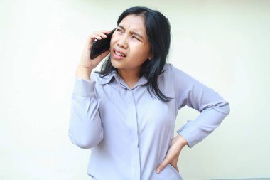 Kafası karışmış Asyalı genç bir kadın cep telefonuyla konuşurken kafasını karıştırıyor. Elini beline uzatmış, izole olmuş, resmi giyinmiş, kuşkulu bir şekilde beyaz bir kadına bakıyor.