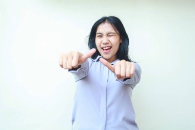 Stüdyoda kendinden emin, heyecanlı Asyalı genç iş kadınının iki parmağını kaldırıp kameraya göz kırpması, onay jesti ve beyaz tişörtlü resmi bir kadın pozu.