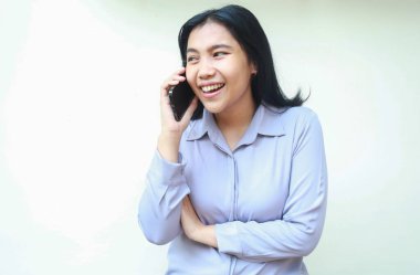 Çekici Asyalı iş kadınının güldüğü bir stüdyo resmi. Cep telefonuyla konuşmaktan zevk alıyor. Kollarını katlamış, başka tarafa bakıyor.