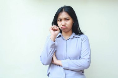 İncinmiş Asyalı genç bir kadın çalışanın yumruk pompası ve kamera karşısında ağlaması üzücü bir şekilde yalnız beyaz arka planda duran resmi mor bir gömlek giymesi.