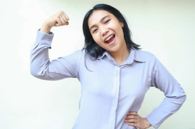 Kaygısız güçlü Asyalı genç iş kadını kollarını kaldırırken kollarını kaldırırken elleri belinde, resmi tişörtü giymiş beyaz arka planda kameraya bakıyor.